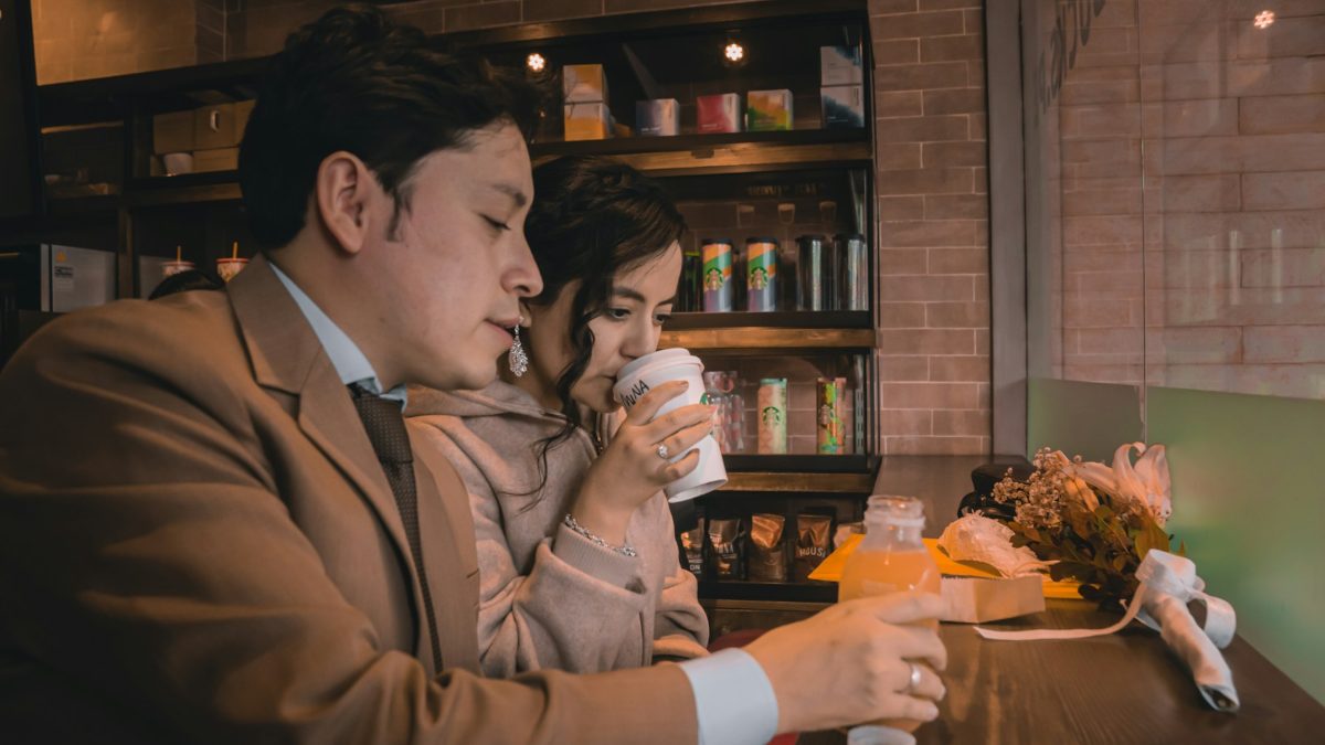 A man and a woman talk across a café table over cups of coffee