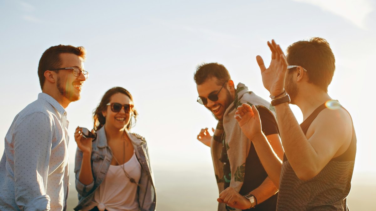 A group of friends laugh together outdoors on a sunny day