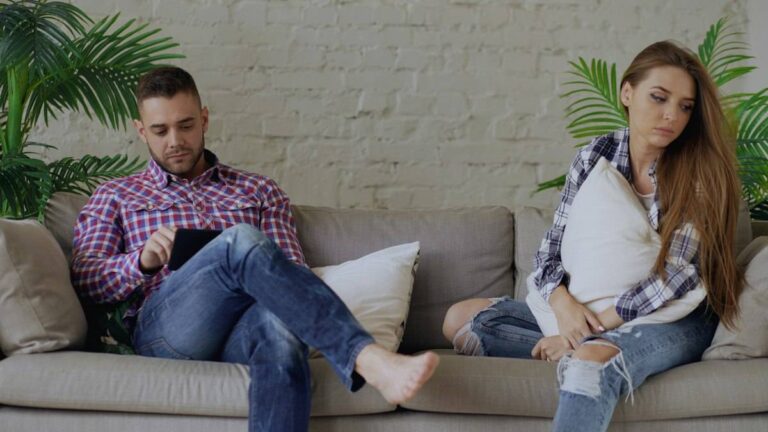 Couple sitting apart on a sofa, each looking at their phone