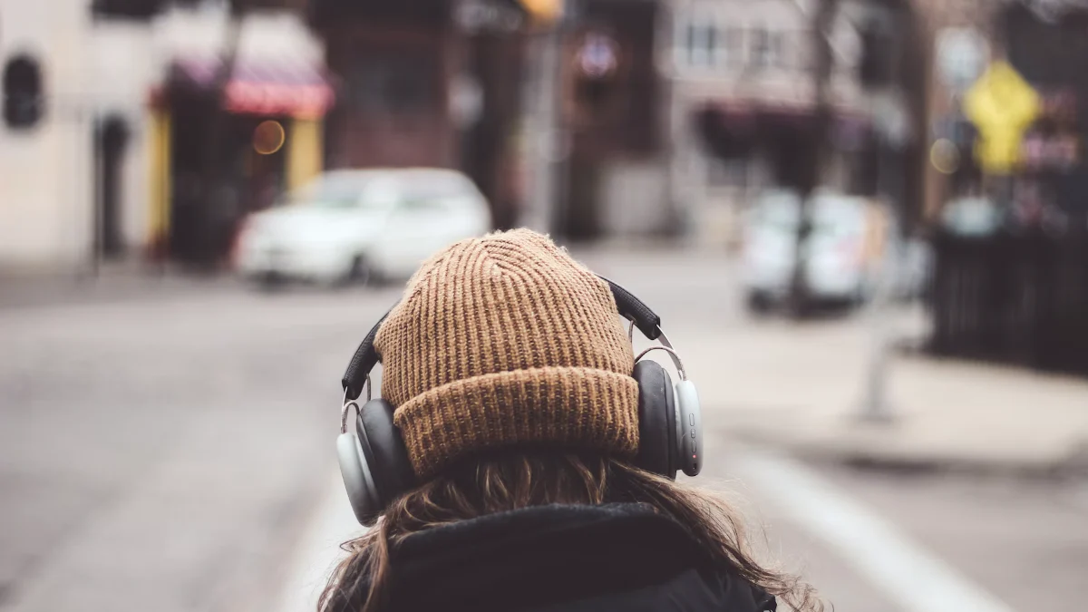 A person in a knitted hat wearing headphones on a city street
