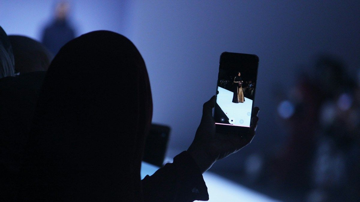 Person filming a woman on a phone during a fashion shoot