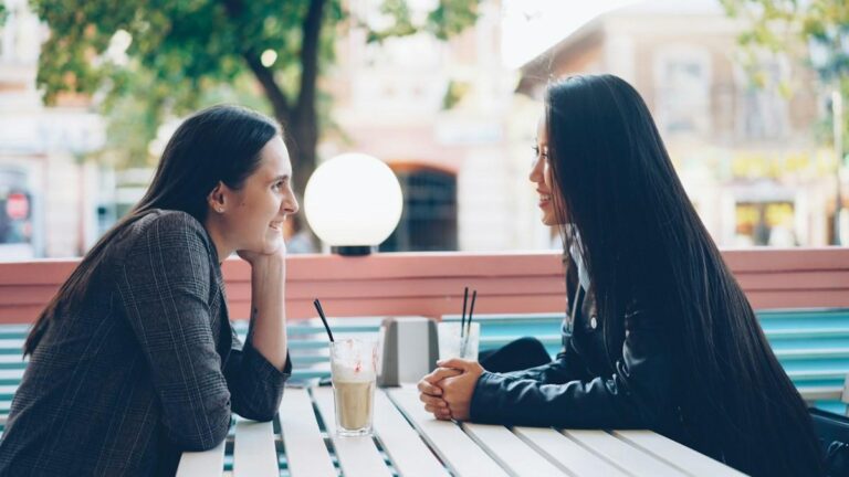 Two women talking across an outdoor cafe table