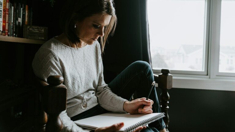 A woman sitting in a chair writing in a notebook