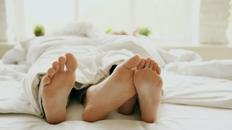 A couple’s feet peeking out from under a white duvet