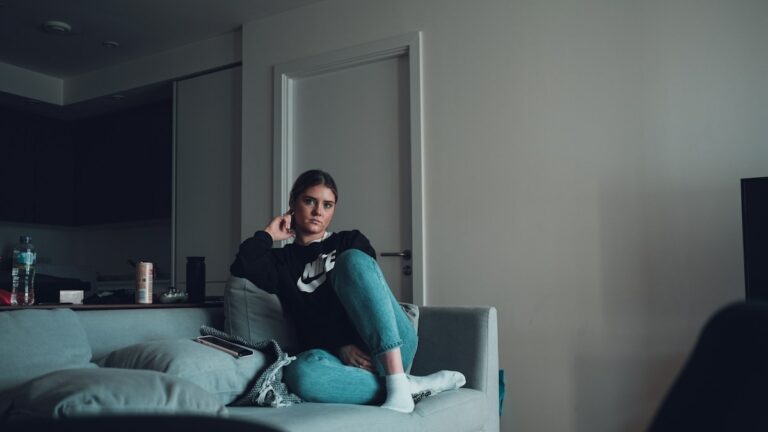 Woman sitting alone on a grey sofa on a quiet evening at home