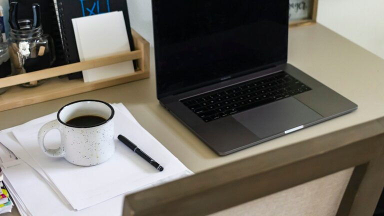 Desk with an open laptop, a mug of coffee and an unfinished note